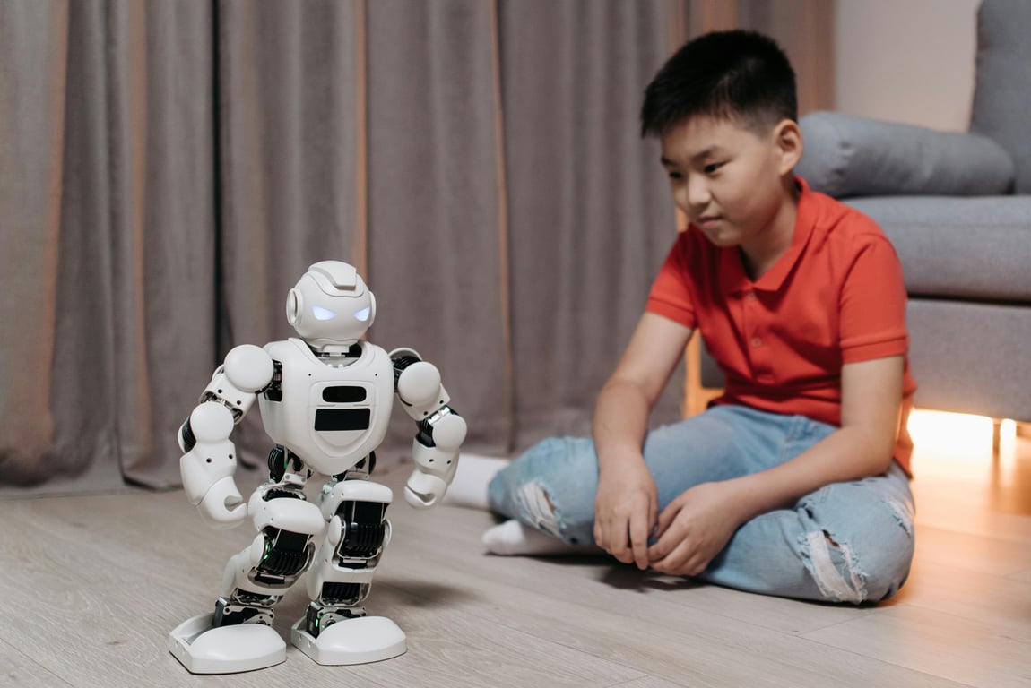 An asian boy sitting on the floor, interacting with a white robot, showcasing innovation and technology.