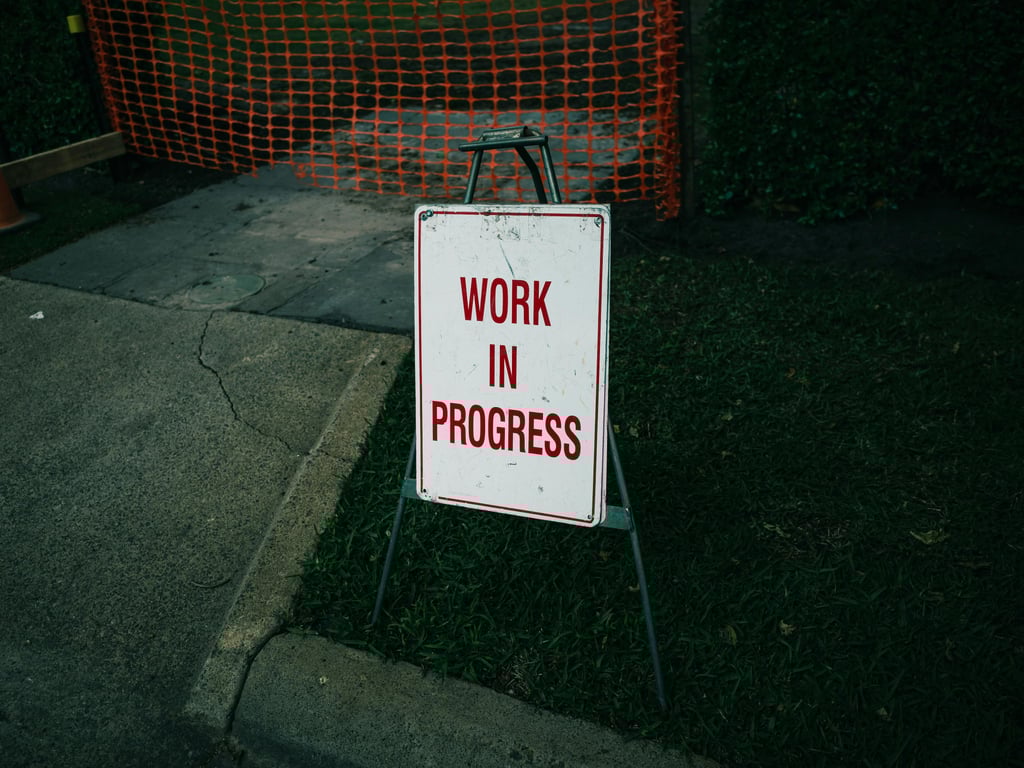 A 'Work in Progress' sign stands on a sidewalk next to safety barriers.