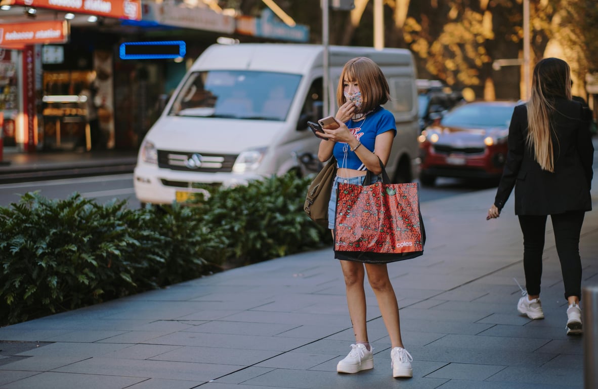 Asian woman wearing face mask and holding shopping bags on a busy street in Sydney.