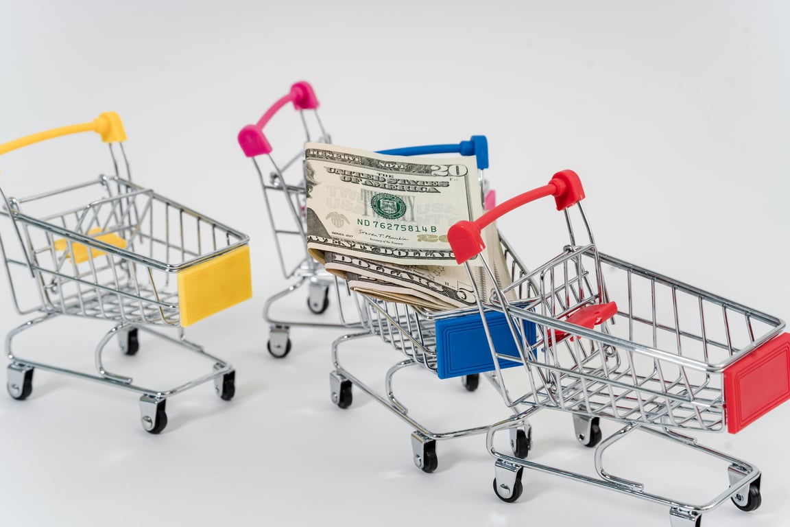 Miniature shopping carts containing dollar bills on a white background.