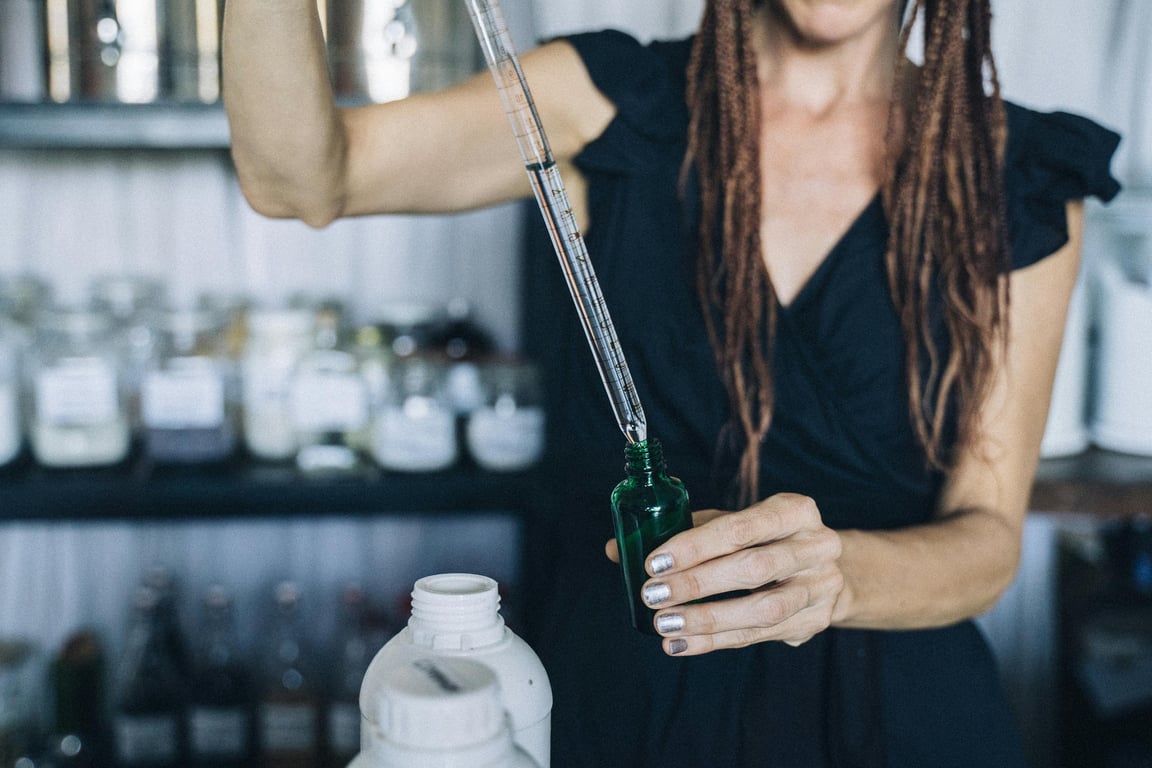 Woman refilling eco-friendly dropper bottle using a pipette in a sustainable setting.