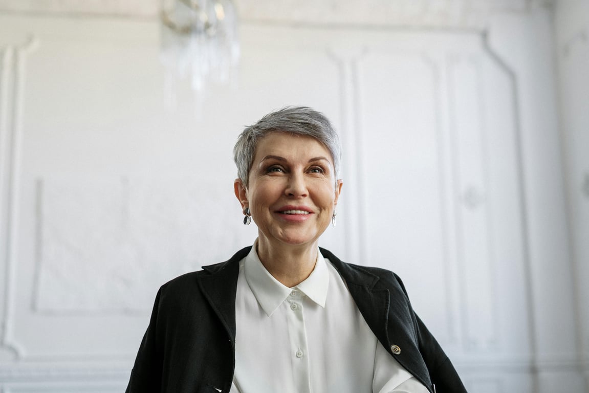 Smiling senior woman in formal attire looking confident in an indoor setting.