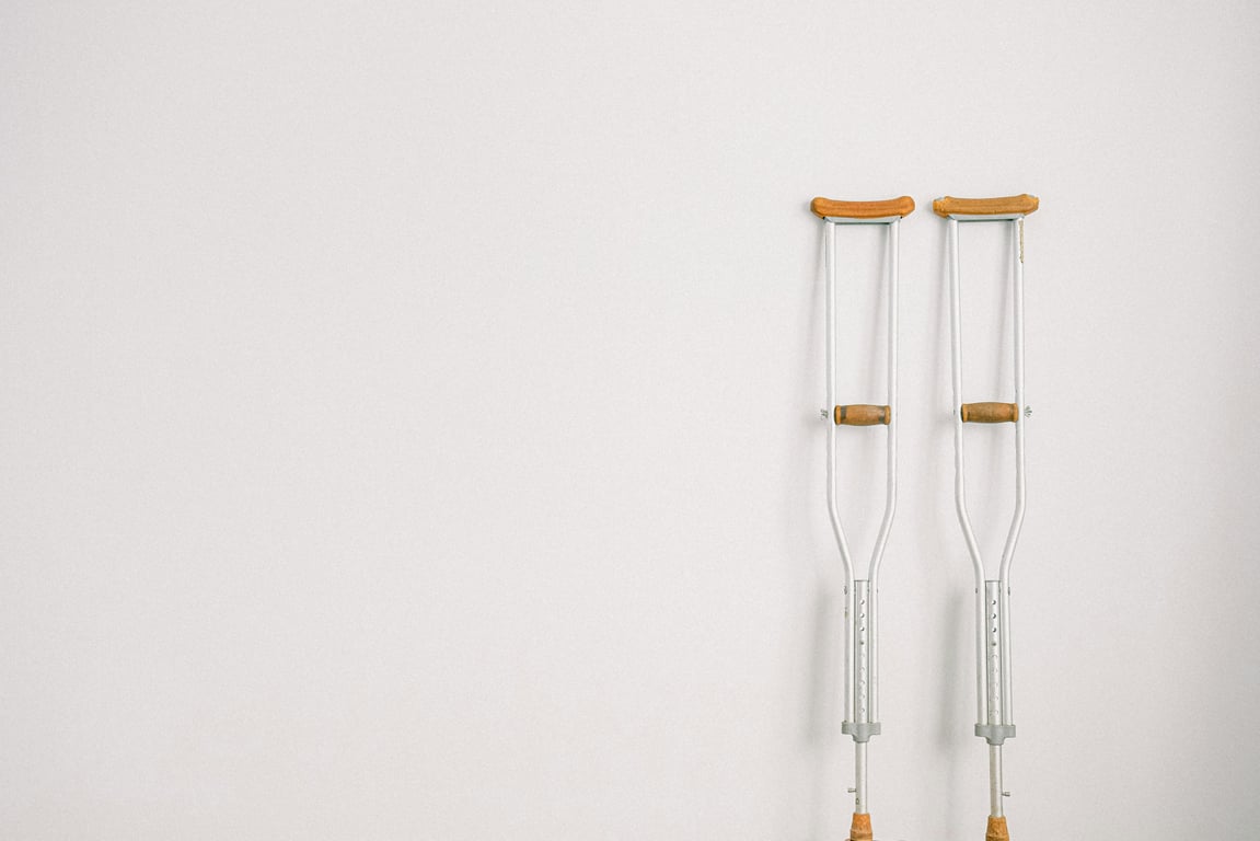 Minimalist image of a pair of crutches leaning on a white wall, symbolizing mobility aid.