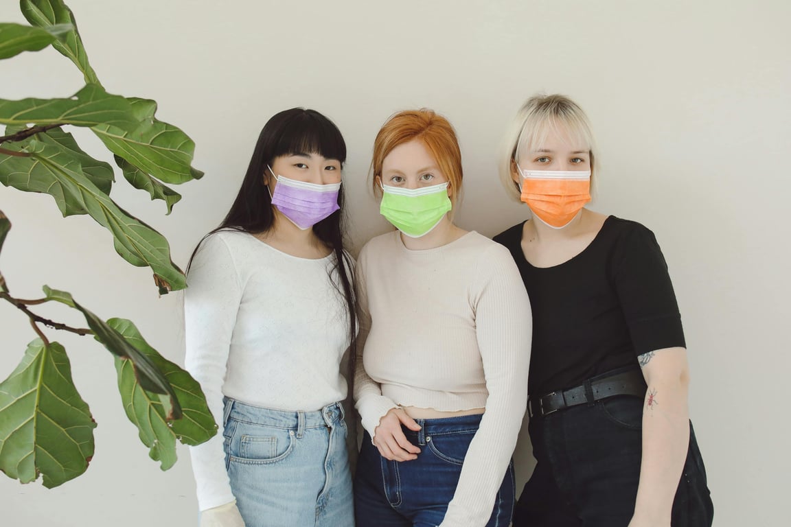 Three women indoors wearing colorful face masks, embracing diversity and safety.