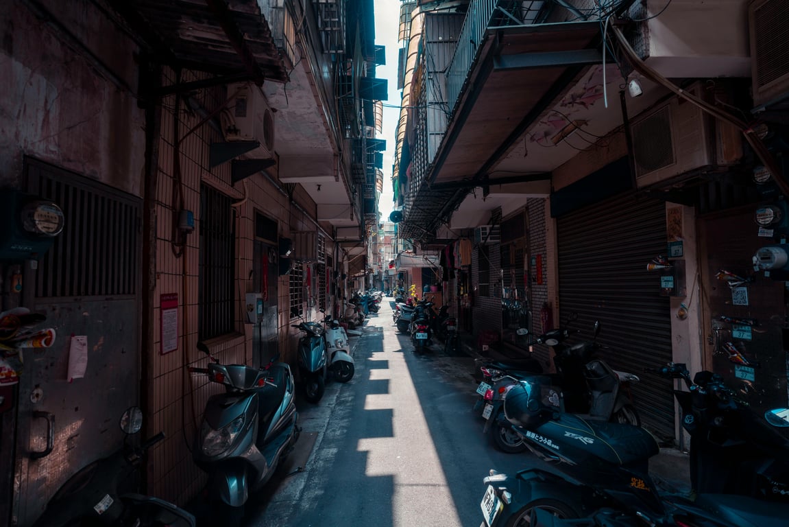 Explore this narrow urban alleyway filled with parked scooters. A typical bustling street scene.