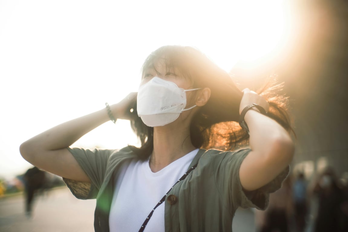 Asian woman enjoys the outdoors in Kowloon while wearing a protective face mask amid a sunset.