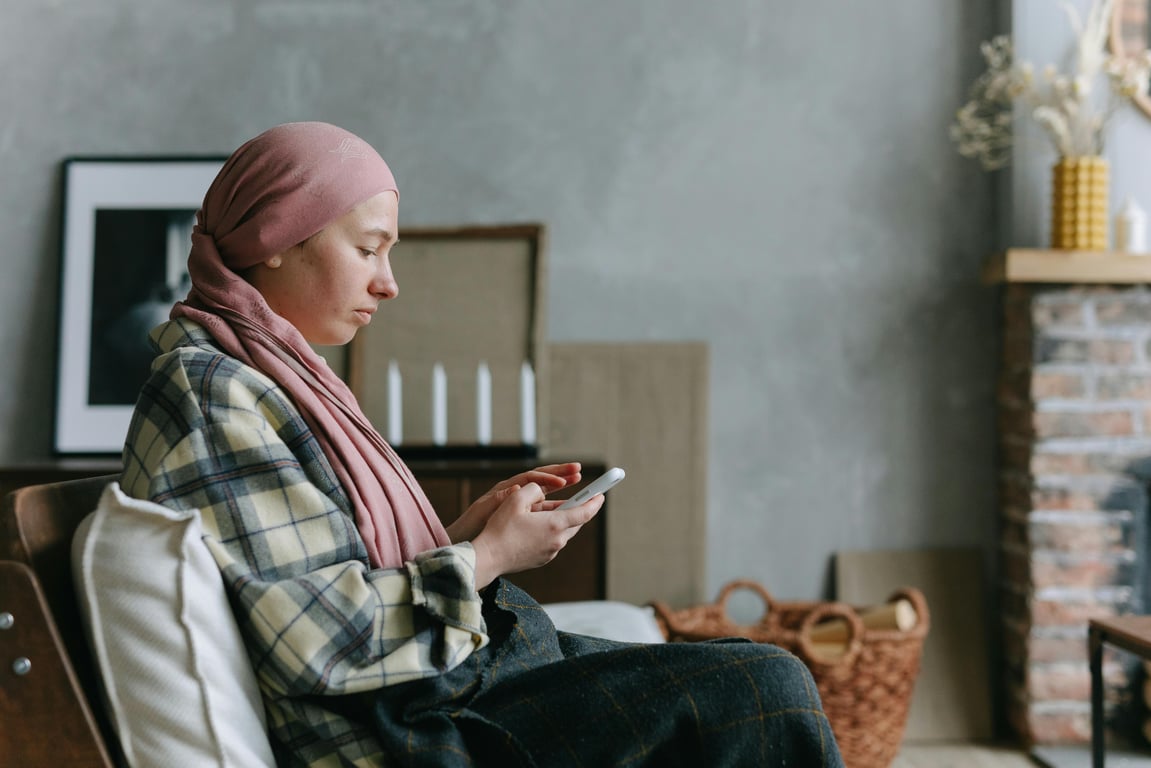 Woman in headscarf using smartphone in a cozy living room setting, reflecting a serene lifestyle.