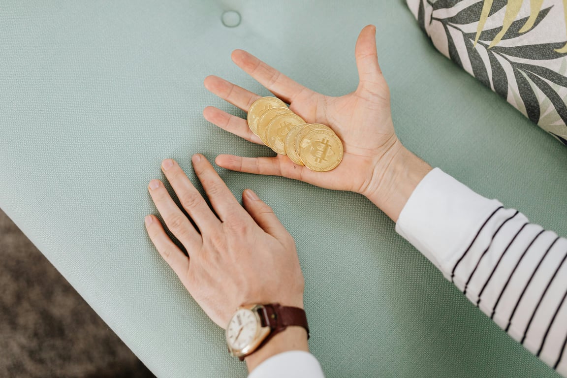 Close-up of hands holding bitcoins on a pastel-colored sofa, showcasing modern finance.