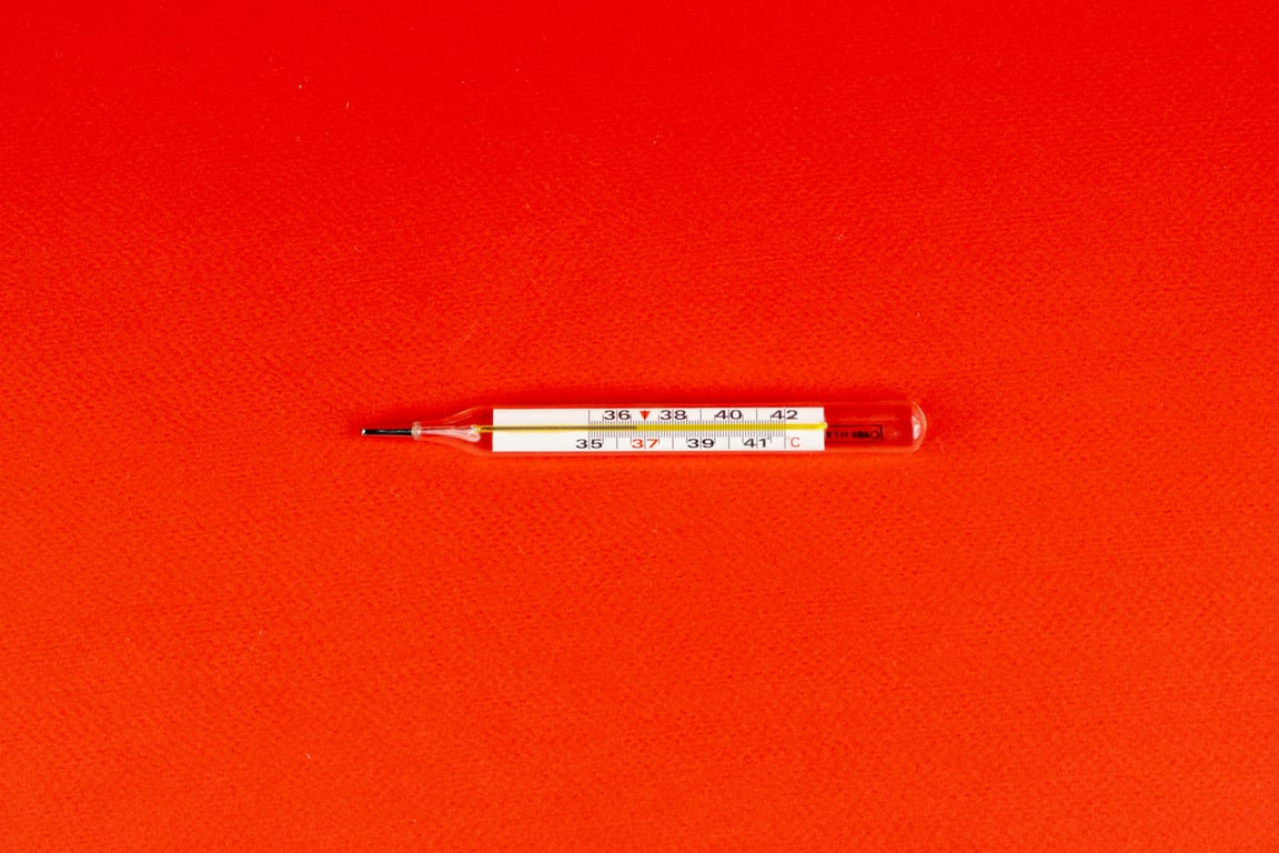 Glass mercury thermometer on a bright red surface, symbolizing health and fever measurement.