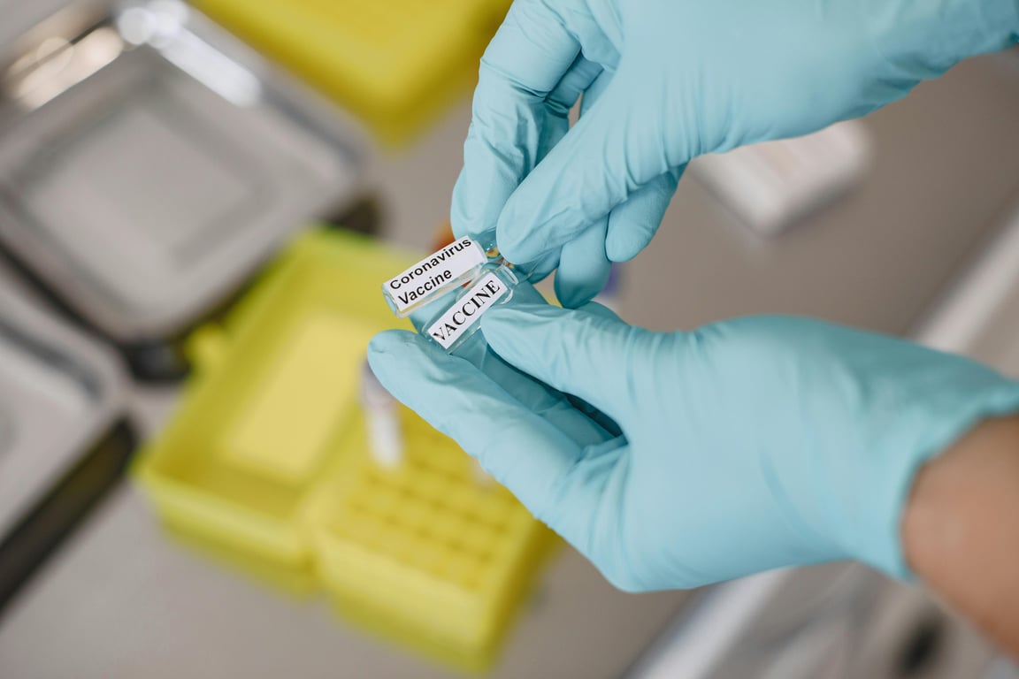Gloved hands holding a labeled coronavirus vaccine vial, representing healthcare and laboratory research.
