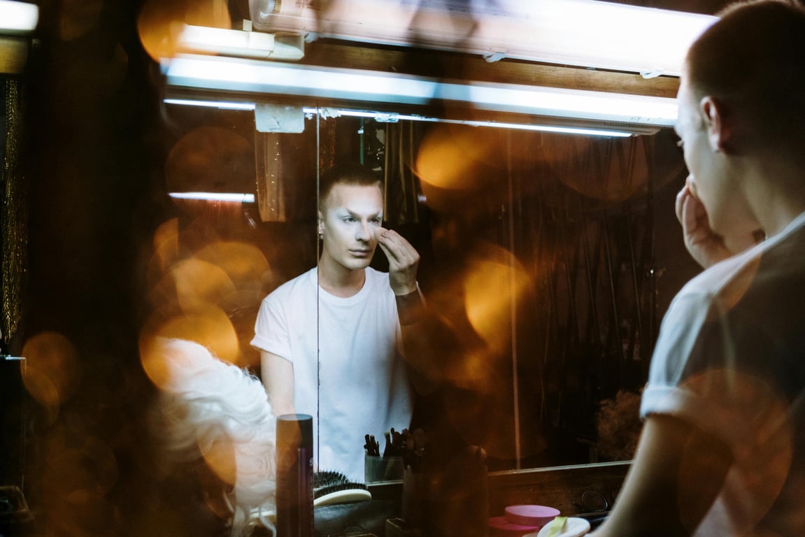 A person applying makeup in front of a mirror, reflecting self-expression and transformation.