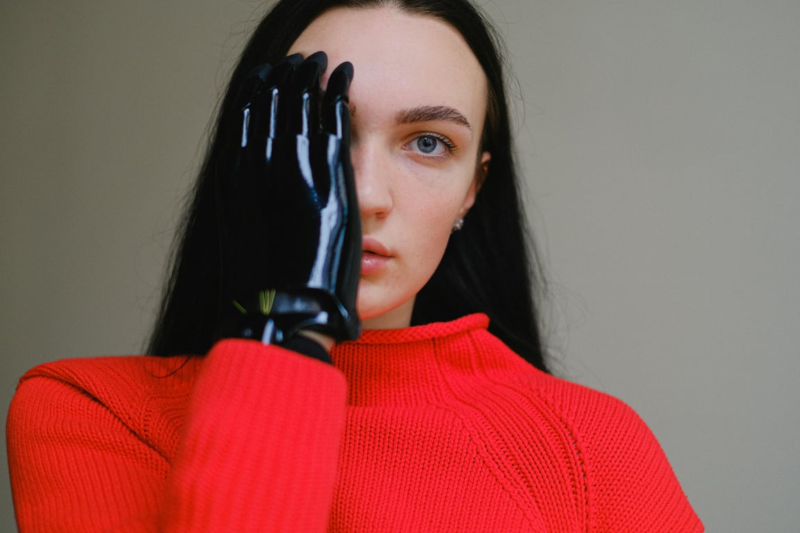 Portrait of a woman with a bionic prosthetic hand wearing a vibrant red sweater.