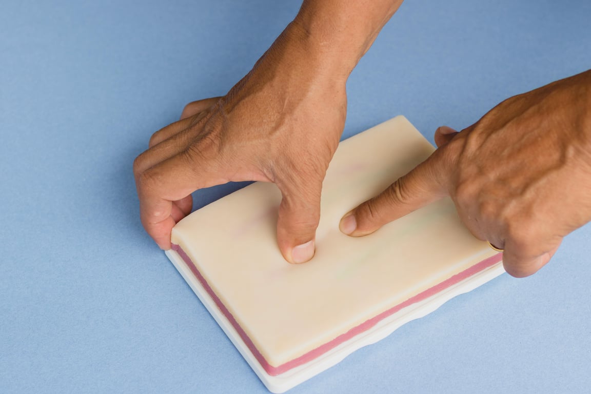 Hands applying pressure to an IV injection training pad, useful for healthcare training.