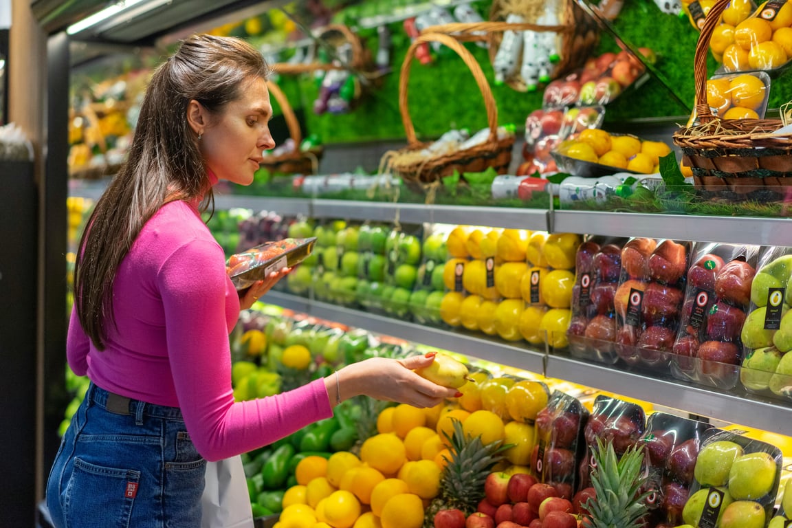 A woman examines fresh fruits in a vibrant grocery store produce section, shopping for healthy options.