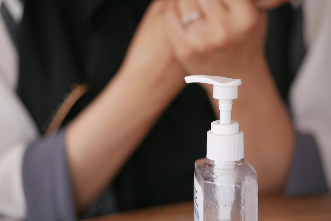 Focused image of a liquid soap dispenser with blurred hands in the background.