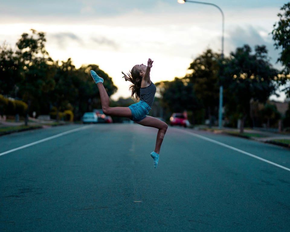 Dynamic shot of a young woman mid-air jump on a quiet urban street at dusk.
