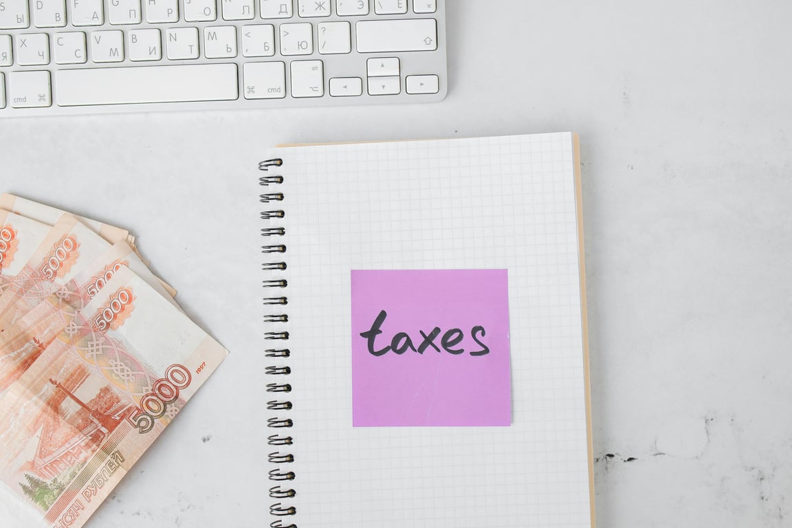 Close-up of a notebook with 'taxes' sticky note, currency bills, and a keyboard symbolizing financial planning.