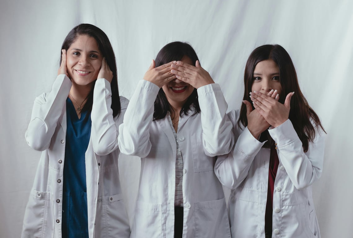 Three women scientists in lab coats posing playfully, symbolizing see no evil, hear no evil, speak no evil.