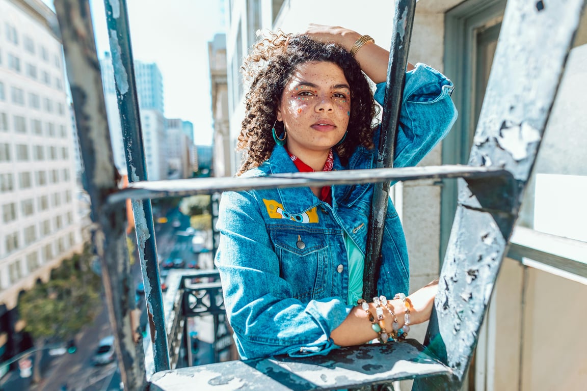 Stylish urban portrait of a young woman on a fire escape, showcasing fashion and confidence.