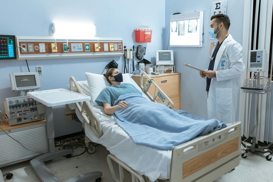 A doctor checking on a patient in a hospital room, both wearing face masks for safety.