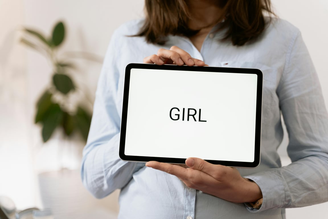 Pregnant woman revealing baby gender on tablet at medical checkup.
