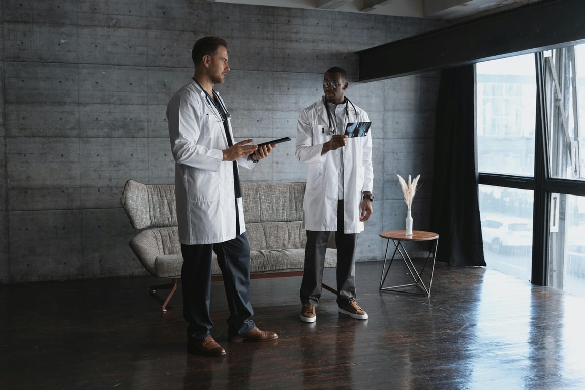 Two doctors reviewing an x-ray image and using a tablet in a contemporary office space with a large window.