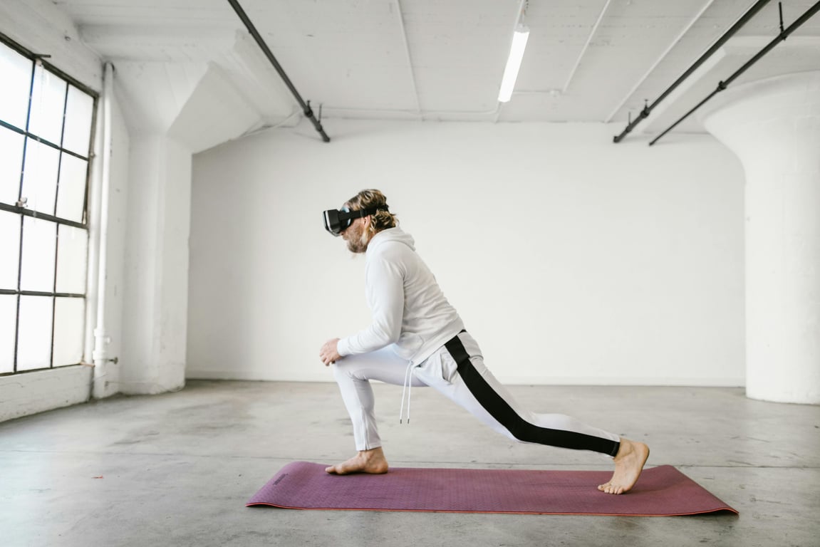 Man wearing VR headset performs yoga stretch indoors on a yoga mat in a brightly lit loft space.