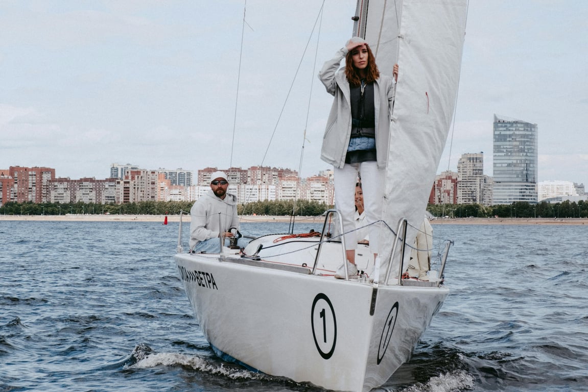 Two people enjoying a sailing adventure on a yacht with a city skyline in the background.
