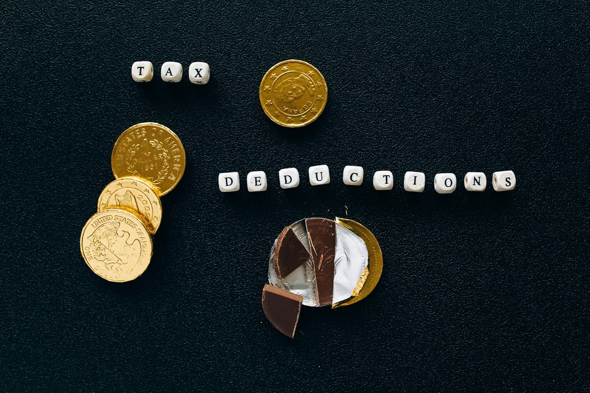 Creative concept of tax deductions using chocolate coins and letter tiles on a black background.