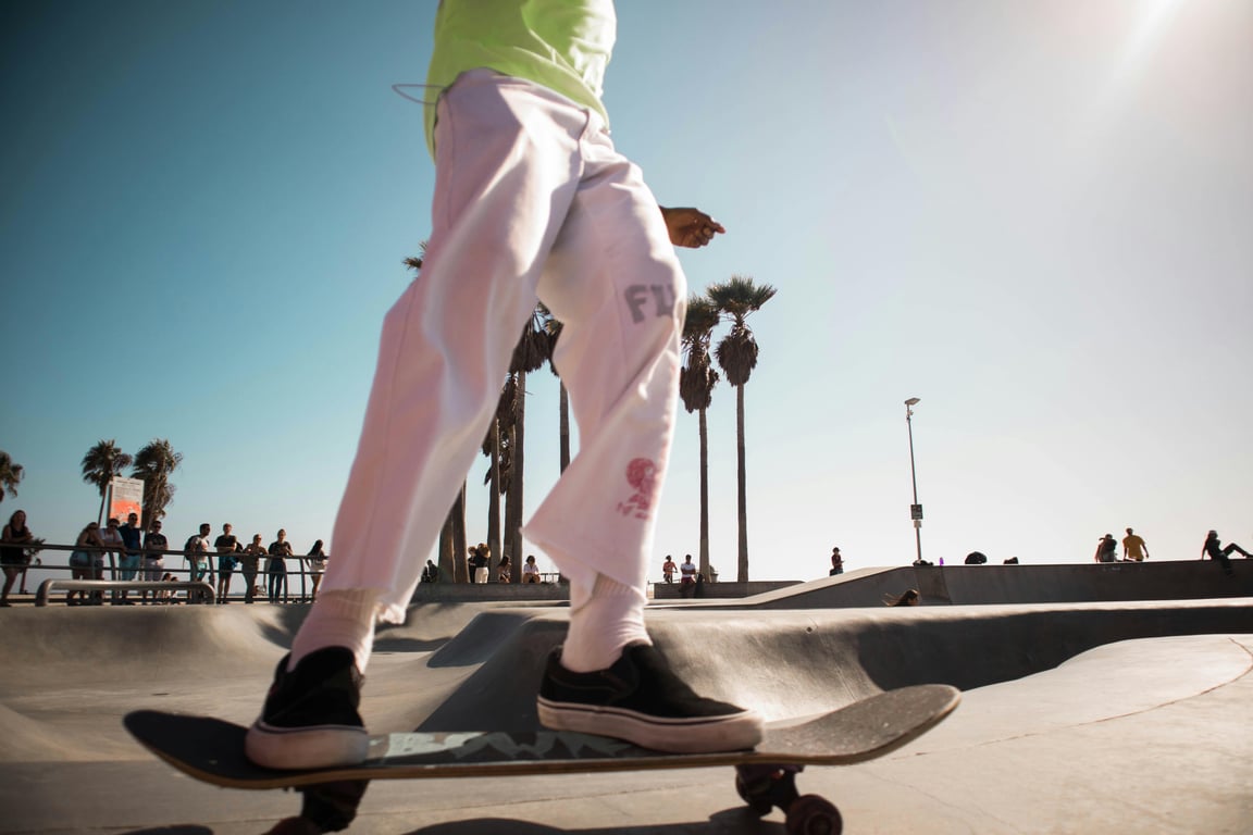 Person skateboarding at a bright skate park with clear blue skies and palm trees.