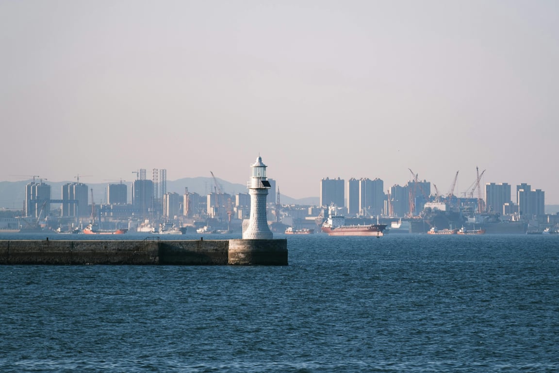 Scenic view of a lighthouse with urban city skyline backdrop over the ocean.