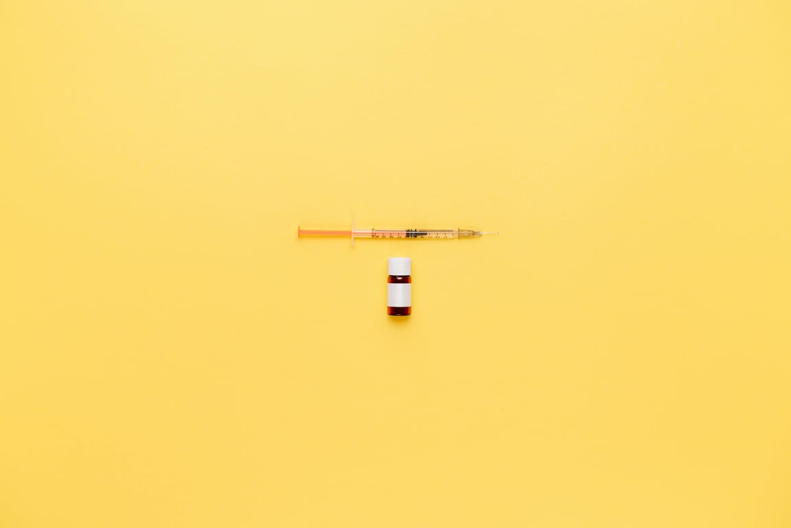 Minimalist image of a syringe and vaccine vial on a vibrant yellow background.