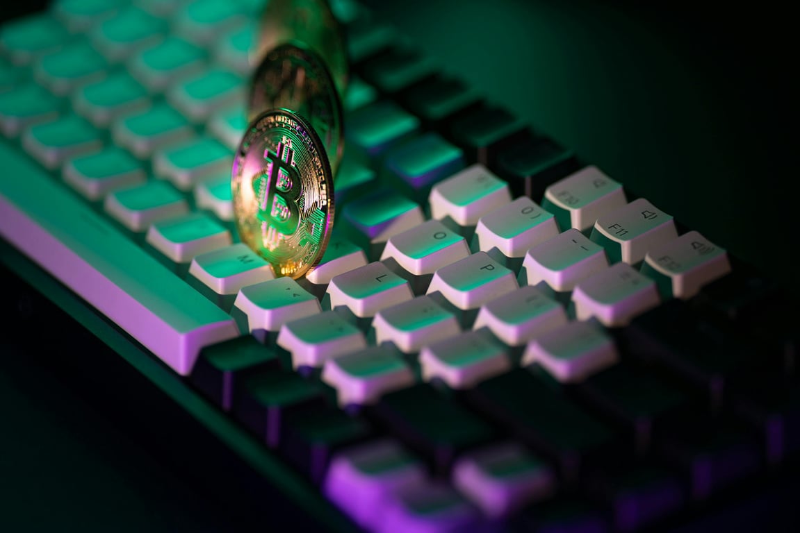 Golden Bitcoin coins on a keyboard with colorful neon lighting. Modern cryptocurrency concept.