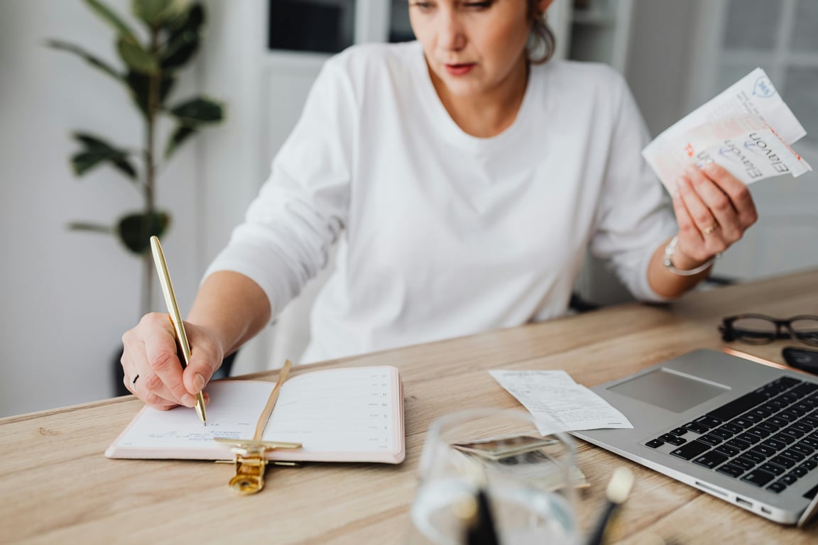 Woman managing finances, writing on notepad, and holding receipts at a desk.