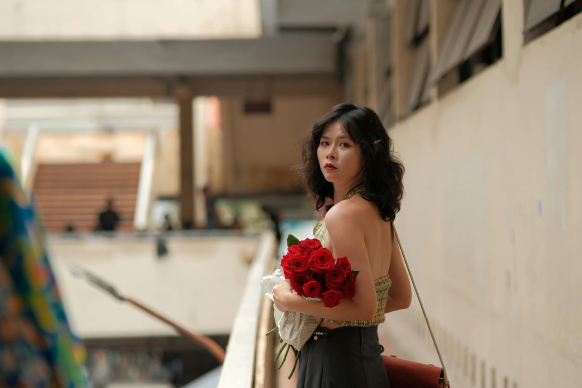 A stylish woman holding a bouquet of red roses in an urban architectural environment.