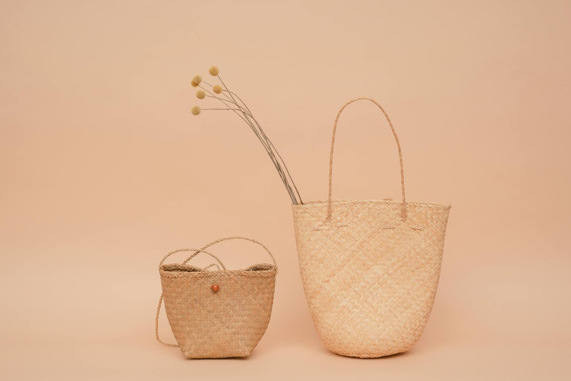 Two woven handbags displayed against a neutral beige background in a studio shot.