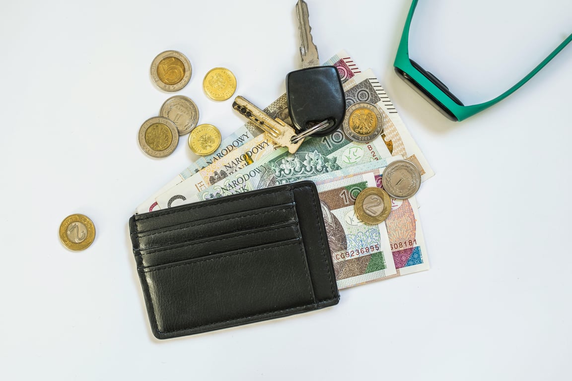 Top view of a wallet, Polish zloty coins, currency notes, and car keys on a white background.