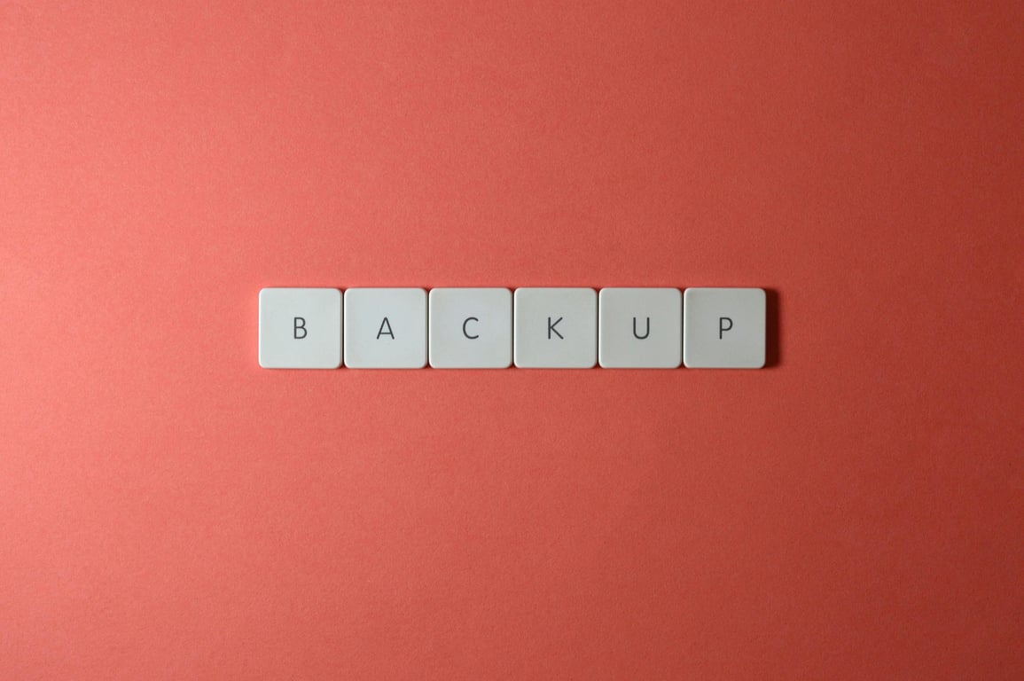 Close-up of keyboard keys spelling 'BACKUP' placed on a coral-colored surface.