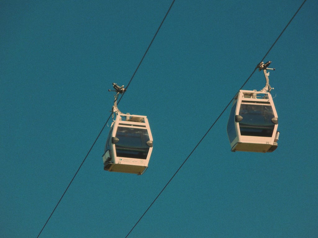 Two white cable cars suspended in the clear blue sky, outdoor transportation.