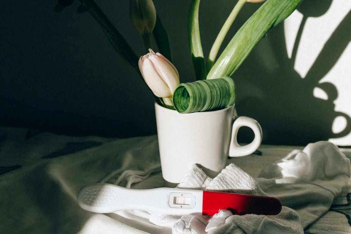 A pregnancy test next to a ceramic mug with tulips, casting dramatic shadows.