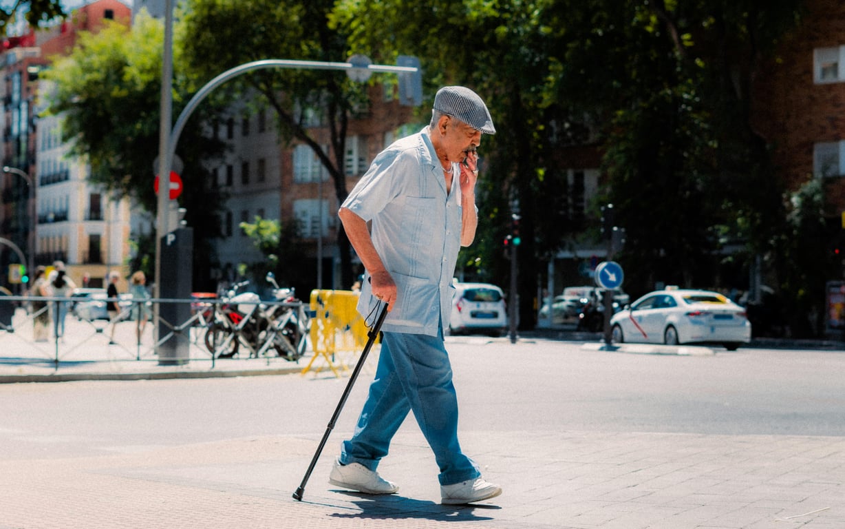 Senior adult using a cane while crossing a street in sunny Madrid.