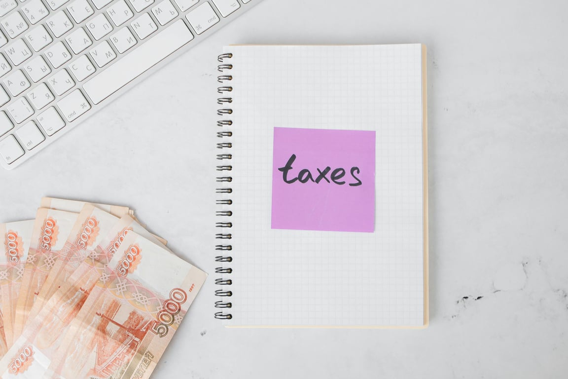 Flat lay image of tax preparation, featuring cash, a notebook, and a computer keyboard on a white surface.