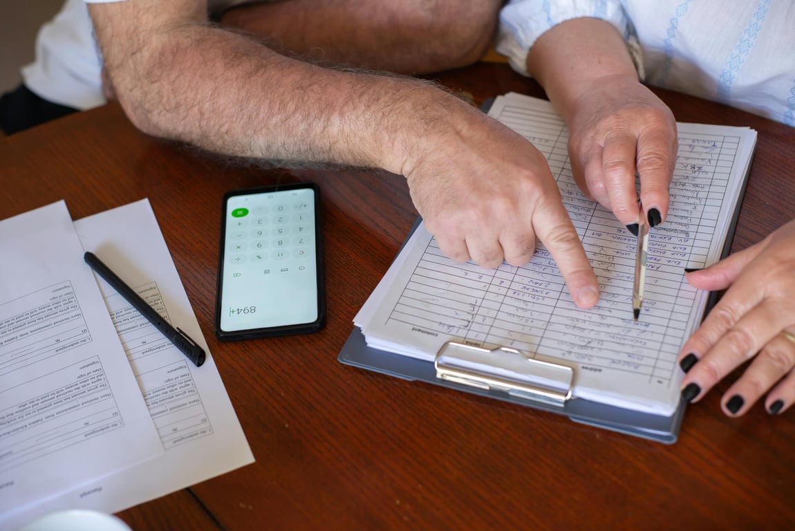 Close-up of hands working on finance planning with documents and a smartphone calculator.