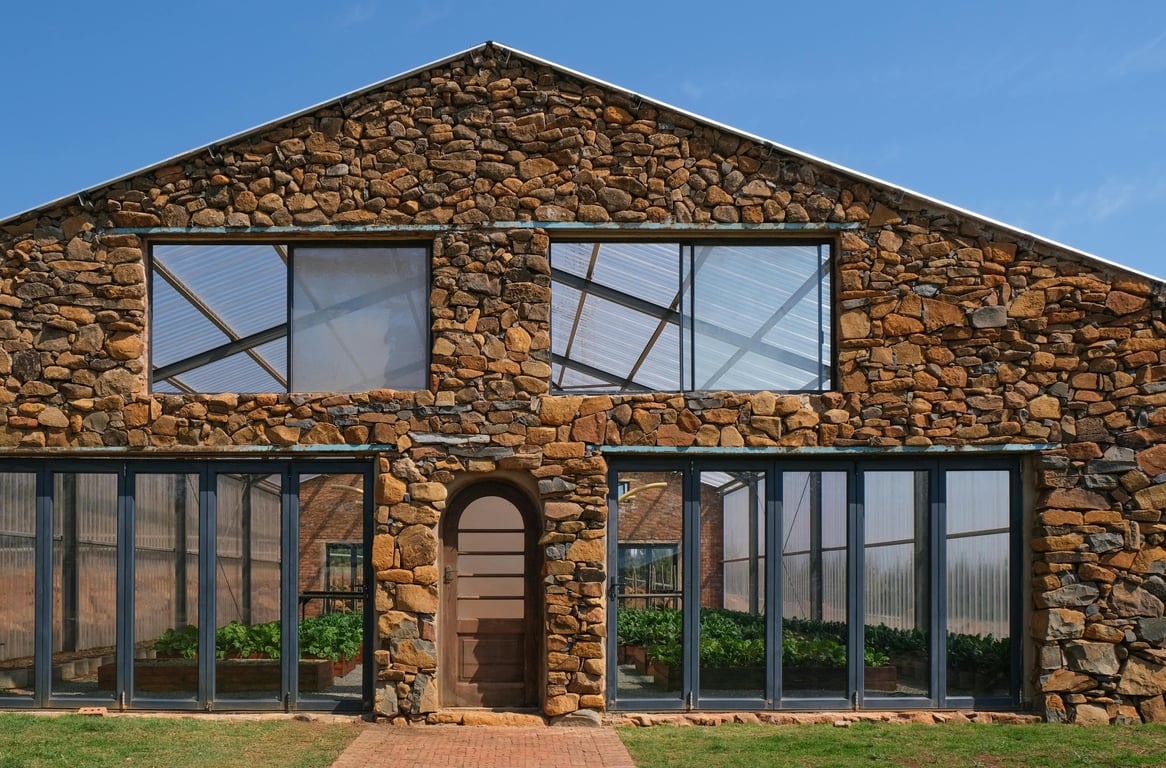 A greenhouse with a rustic stone exterior and glass windows suitable for cultivating plants.