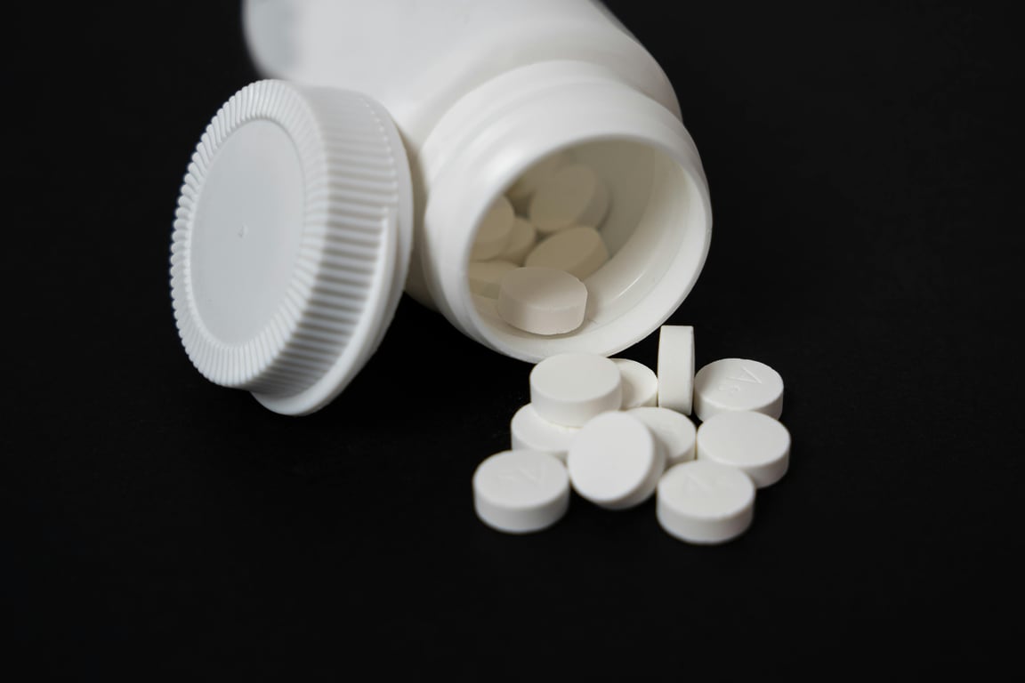 Close-up of white tablets spilling from a plastic container on a black background, highlighting medication.