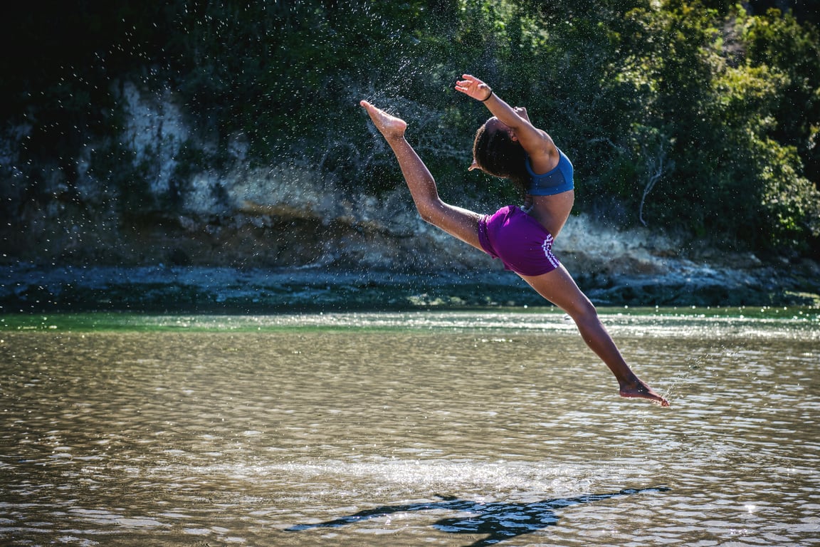 Young woman leaps in front of a river, showcasing flexibility and energy.