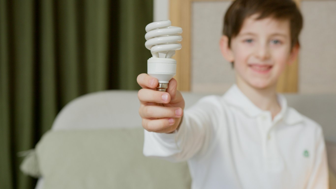 Young boy with light bulb promoting energy efficiency indoors.