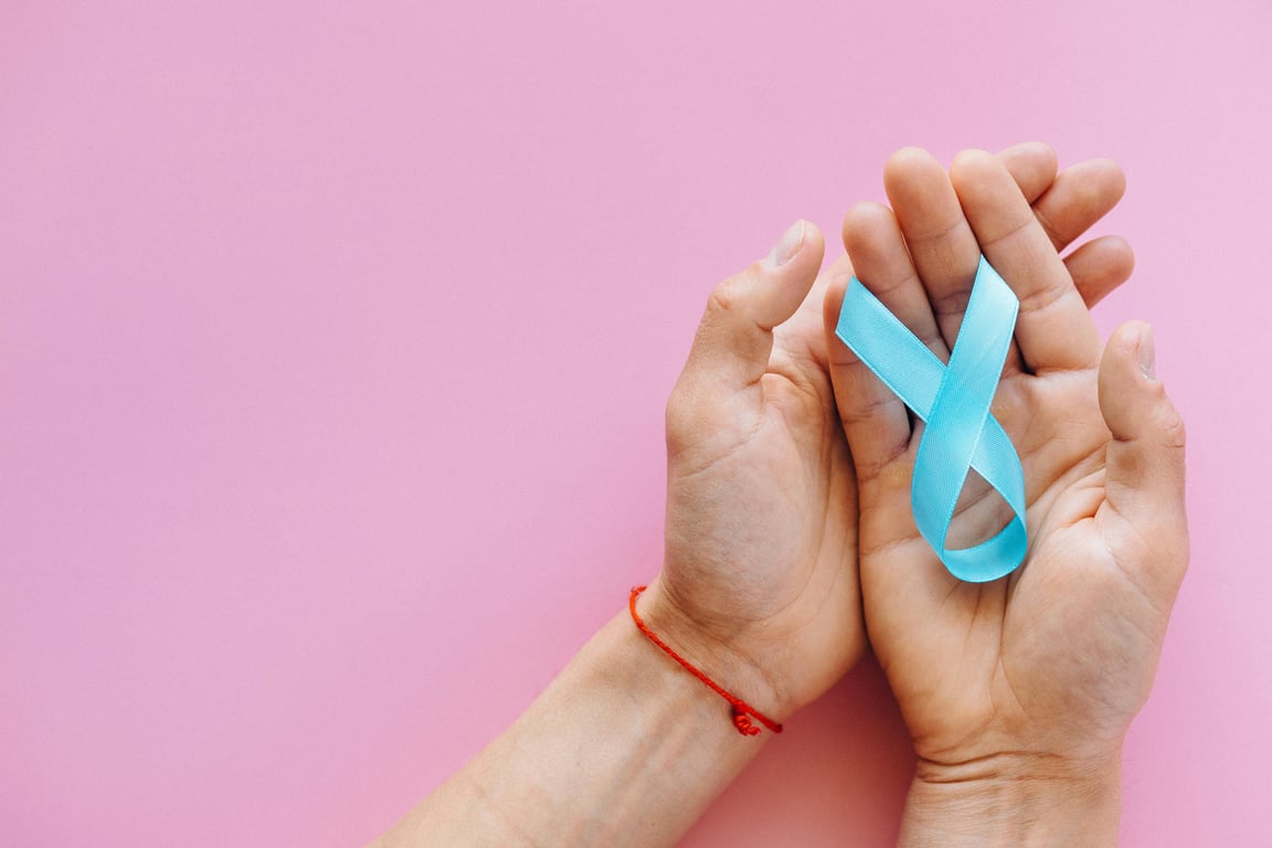 Hands holding a blue ribbon on a pink background symbolizing awareness and support.