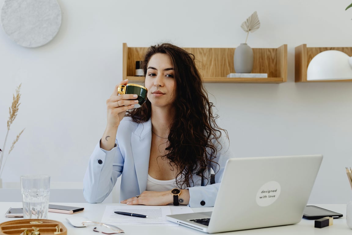 Confident businesswoman enjoying a cup of coffee while working on her laptop in a chic office setting.