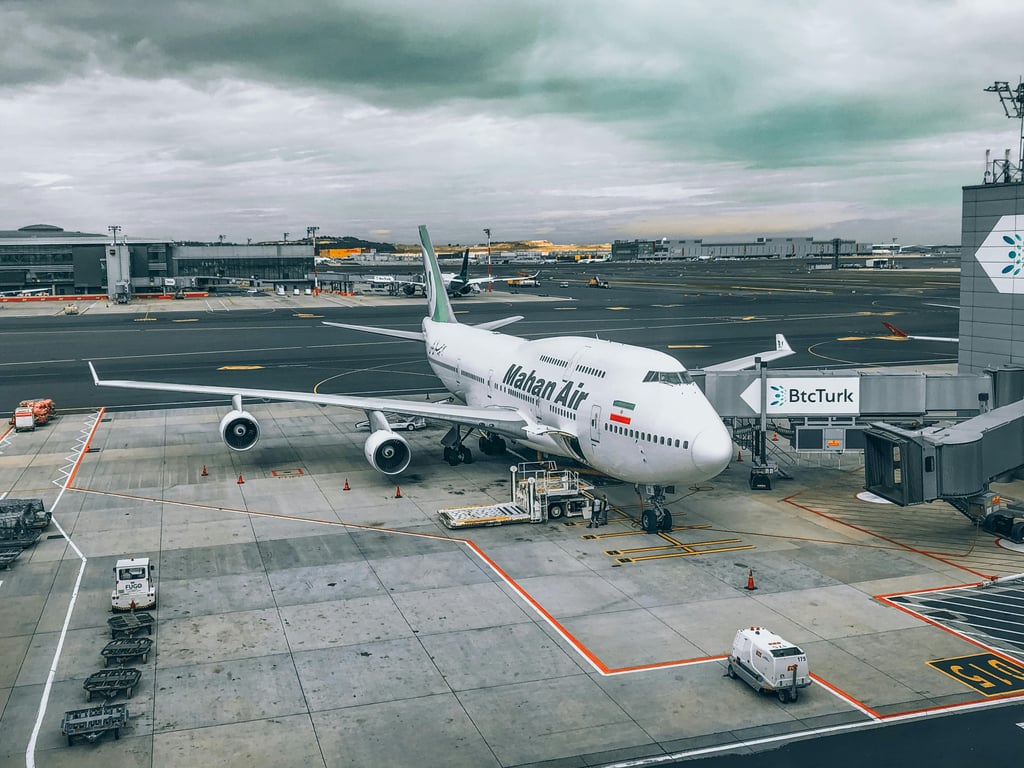 A Mahan Air Boeing 747 aircraft parked at a bustling airport terminal under cloudy skies.